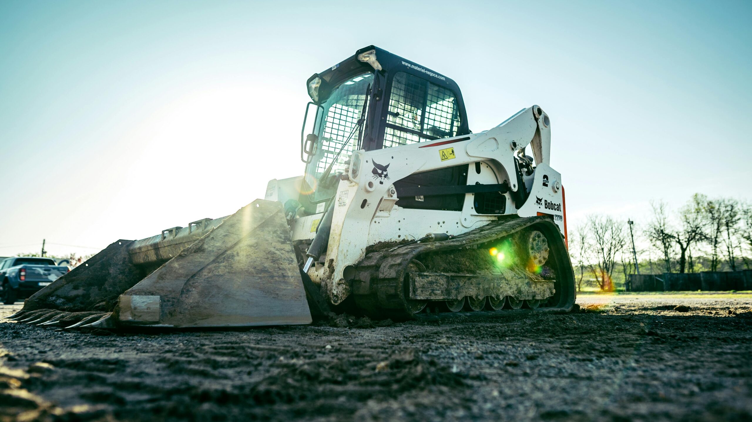 A skid steer loader on a construction site with bright sunlight in the background.